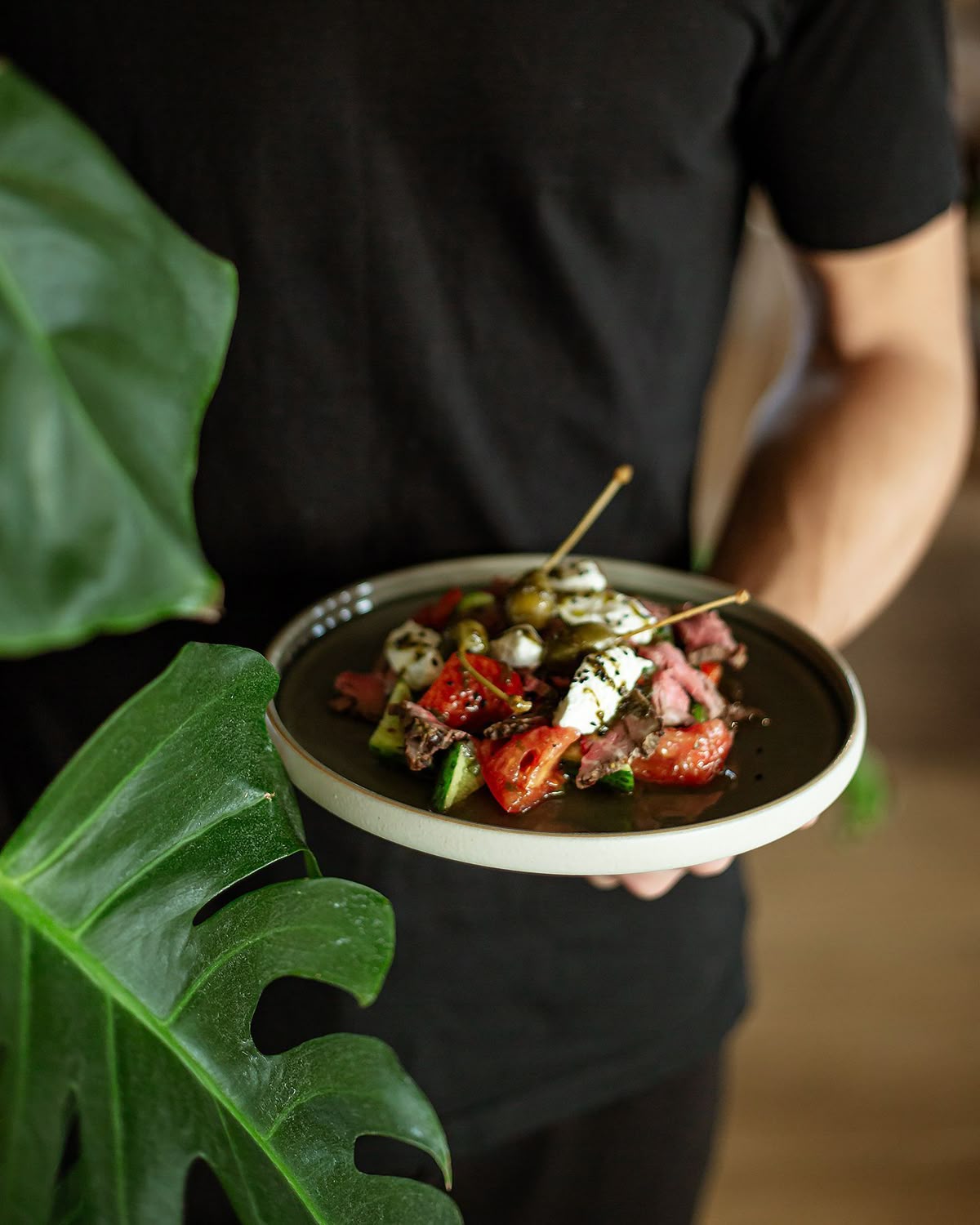 Fresh salad plate held next to tropical leaves